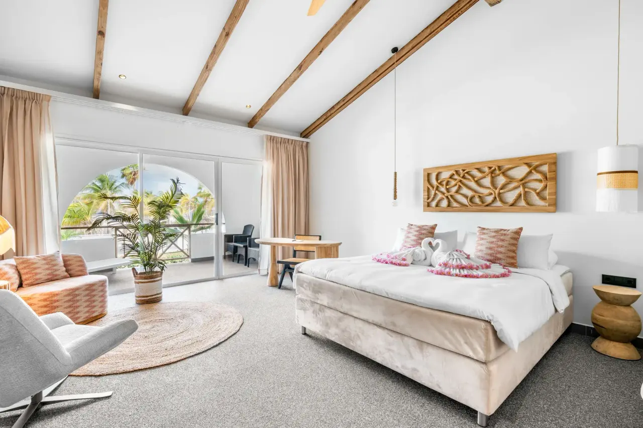 King Suite Ocean van Van der Valk Bonaire met bed en een boogvormige opening naar het balkon