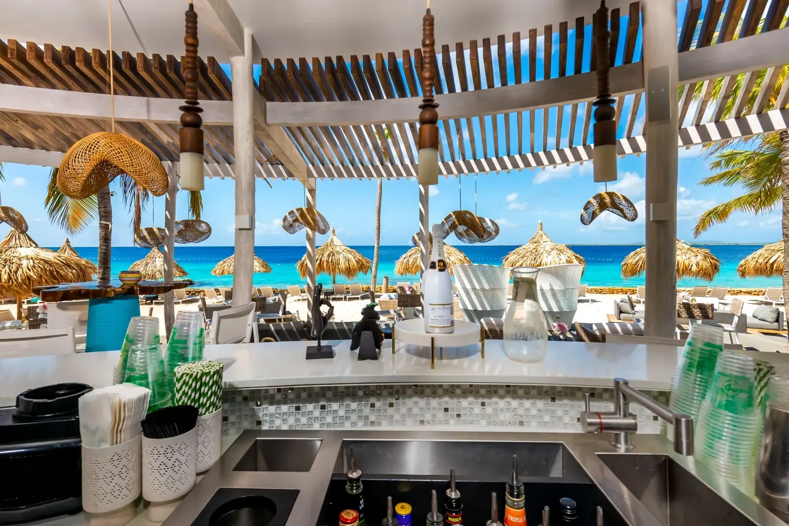 Uitzicht vanachter de toog van Palm Beach Bar op het strand en de palapas van Van der Valk Bonaire